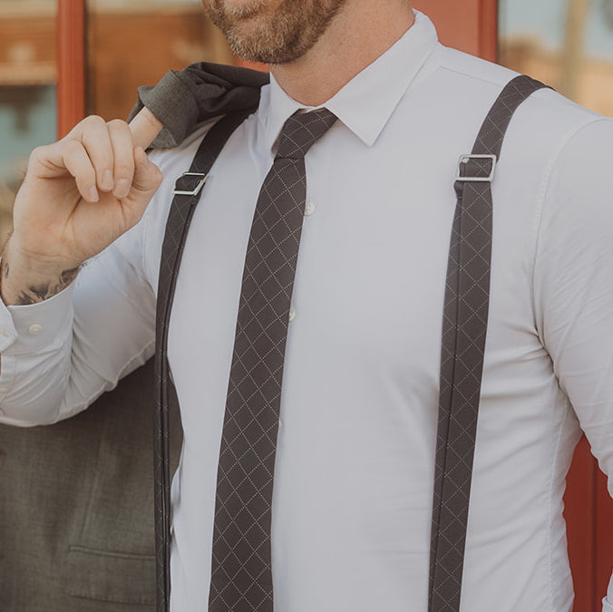 Man adjusting a tie with suspenders over a white shirt against a blurred background
