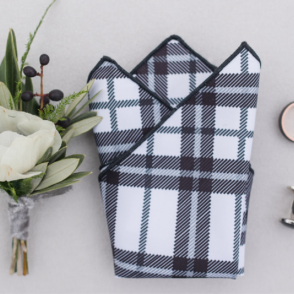 Black and white plaid pocket square folded on table with flowers next to it