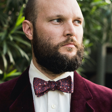 man wearing a red floral bow tie and red tux in an outdoor setting.