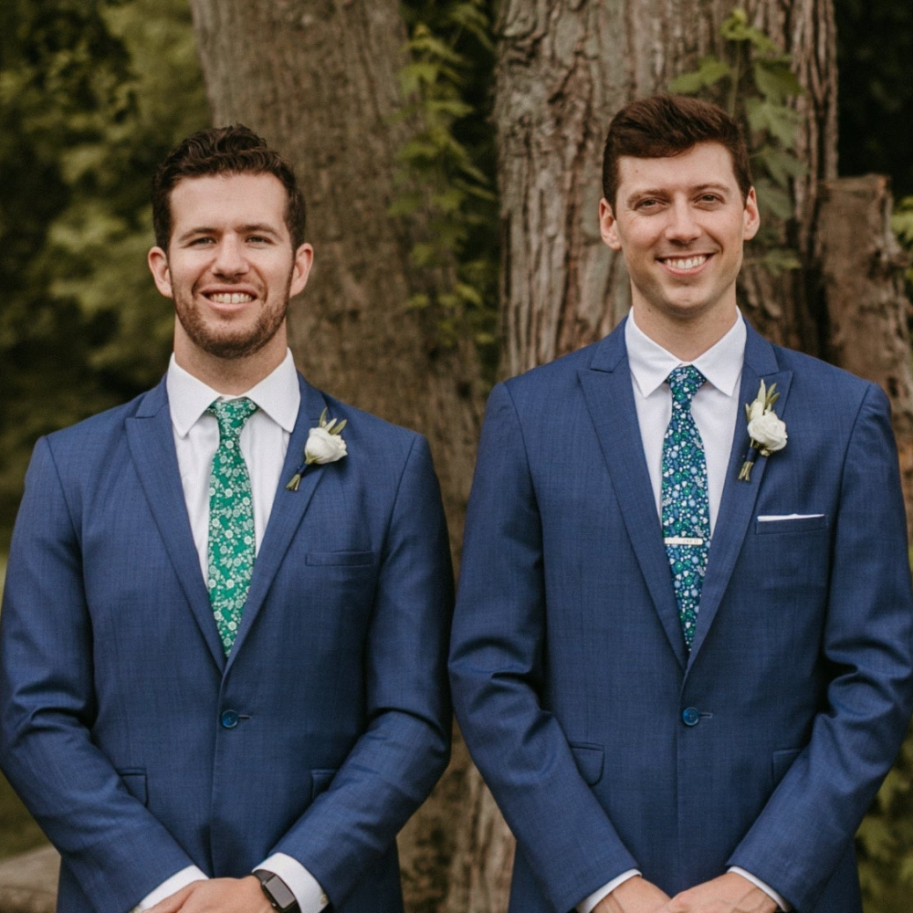 two men wearing customized floral neckties at an outdoor wedding